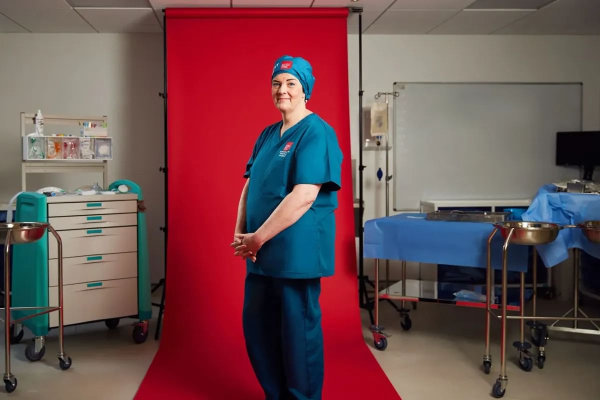 Allied Health student n scrubs stands confidently in front of a vibrant red backdrop.