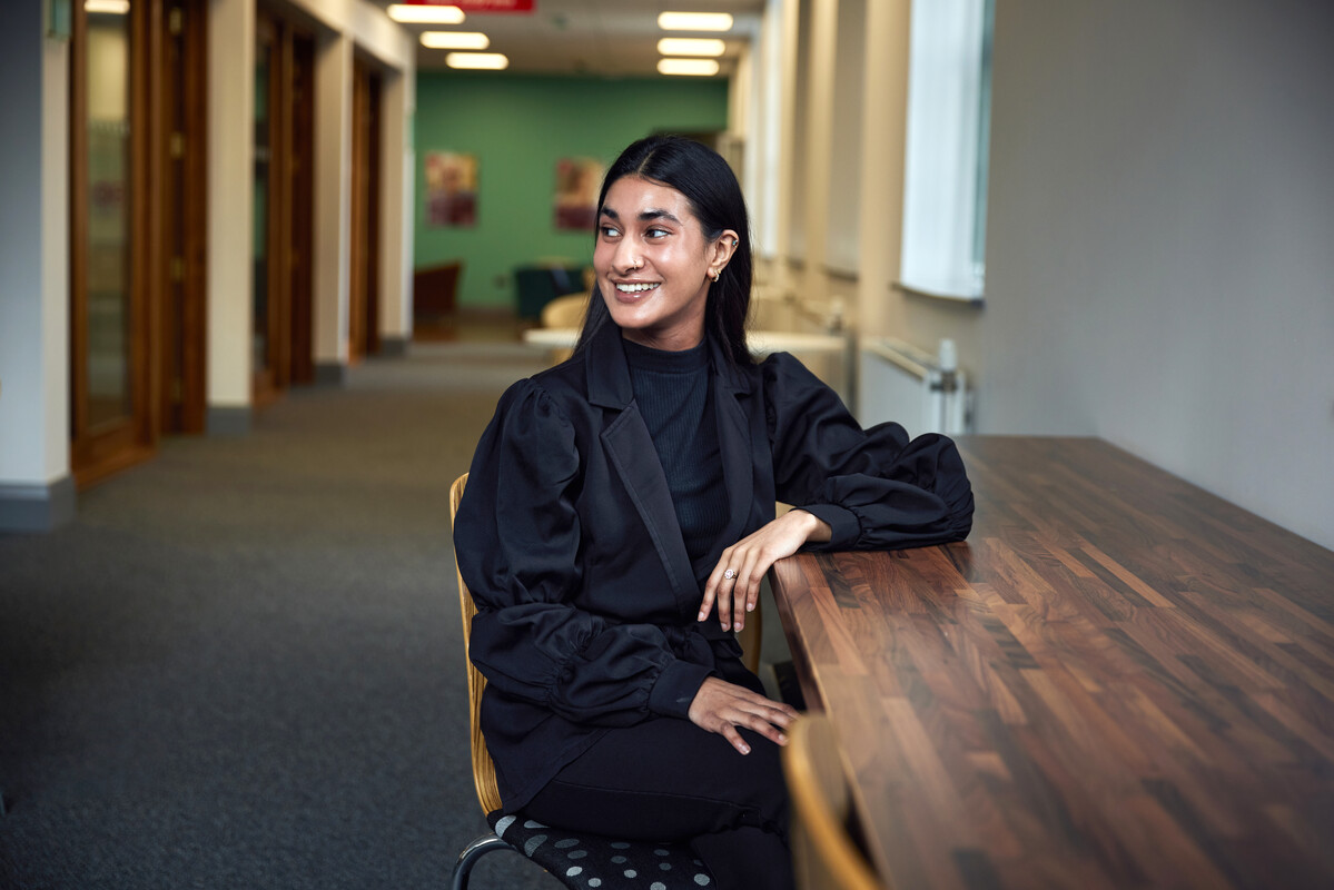 Student Sumaya Khan sits at a table and smiles at the postgraduate centre in Treforest