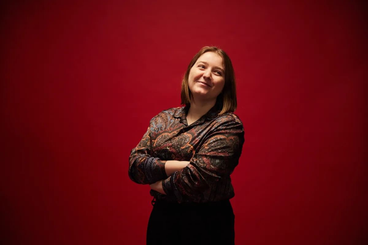 Computing graduate, Niamh, stands for a profile photo in front of a red backdrop