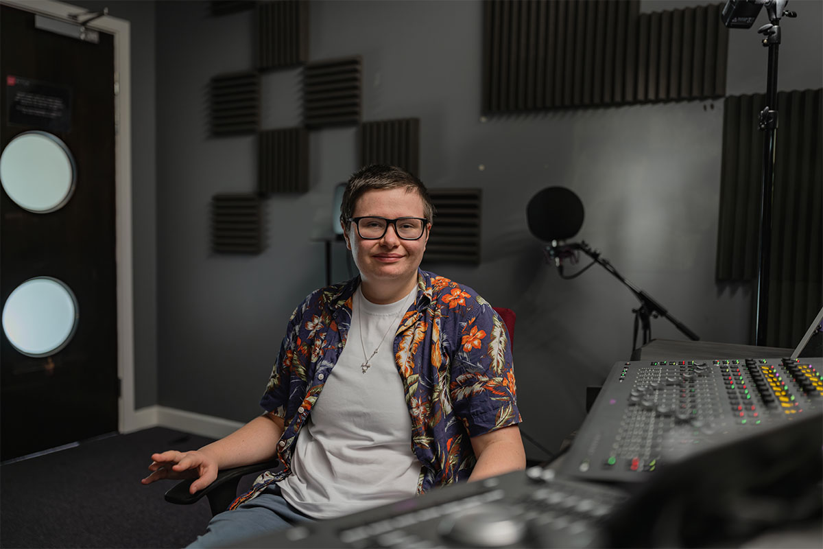 Film student, Edison, smiles at camera whilst sat in a film studio at Cardiff campus