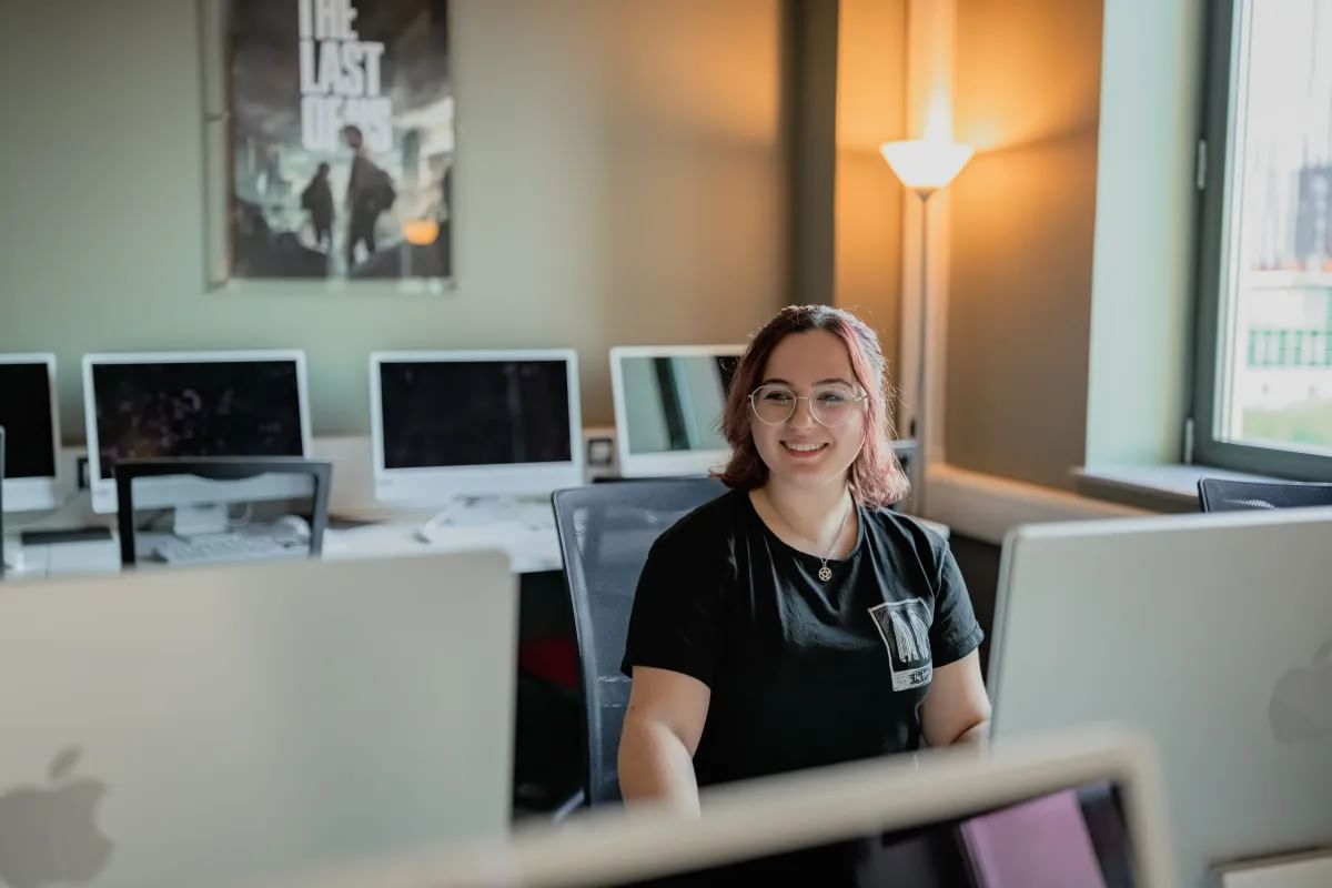 Film student, Amy, smiles at the camera whilst sat at a desk with computers