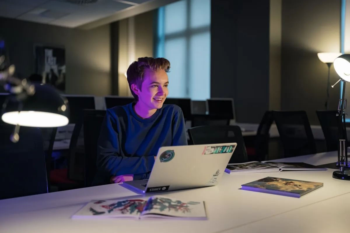 Tom  sits at a desk, focused on his laptop, surrounded by a cozy workspace.