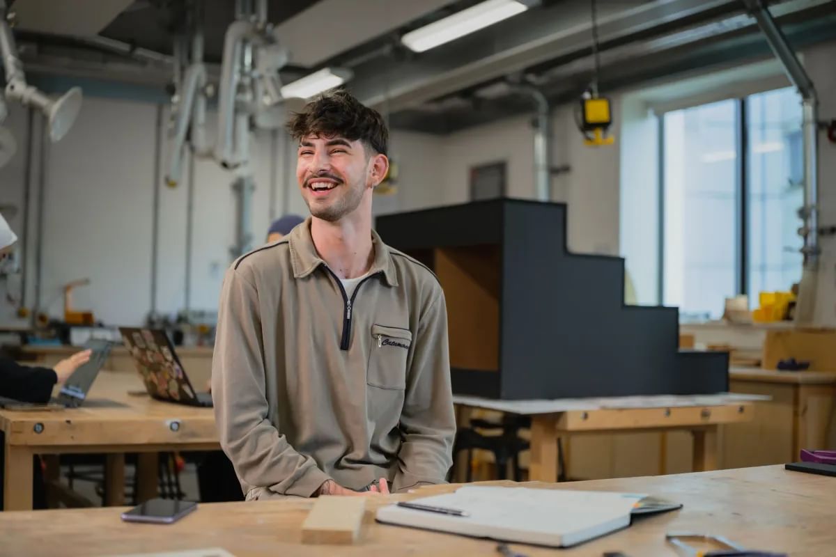 Interior Design student Filip sat in a workshop smiling whilst looking away from the camera
