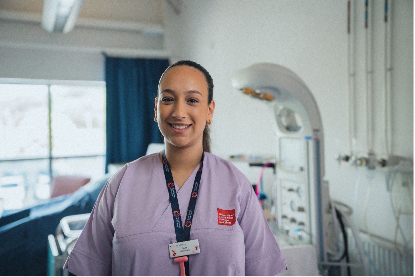 Midwifery student Fiona smiles at camera, wearing purple scrubs in the clinical simulation centre