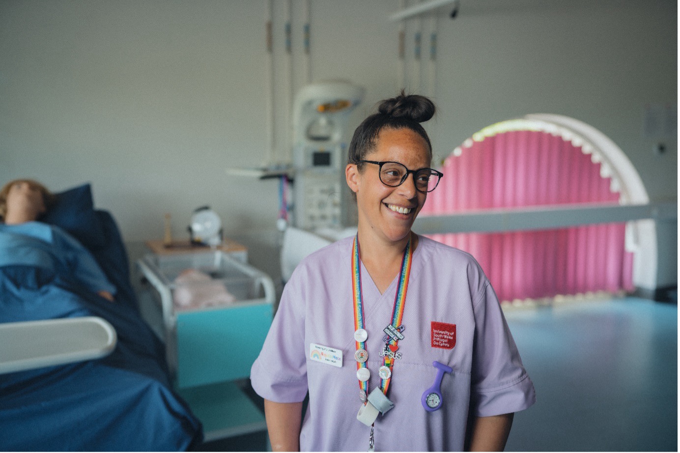 Midwifery student Niquita smiles at camera, wearing purple scrubs in the clinical simulation centre