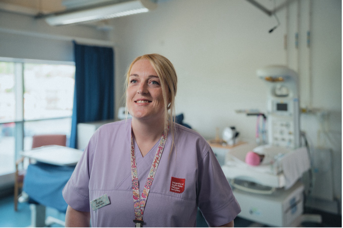 Midwifery student Sophie smiles at camera, wearing purple scrubs in the clinical simulation centre