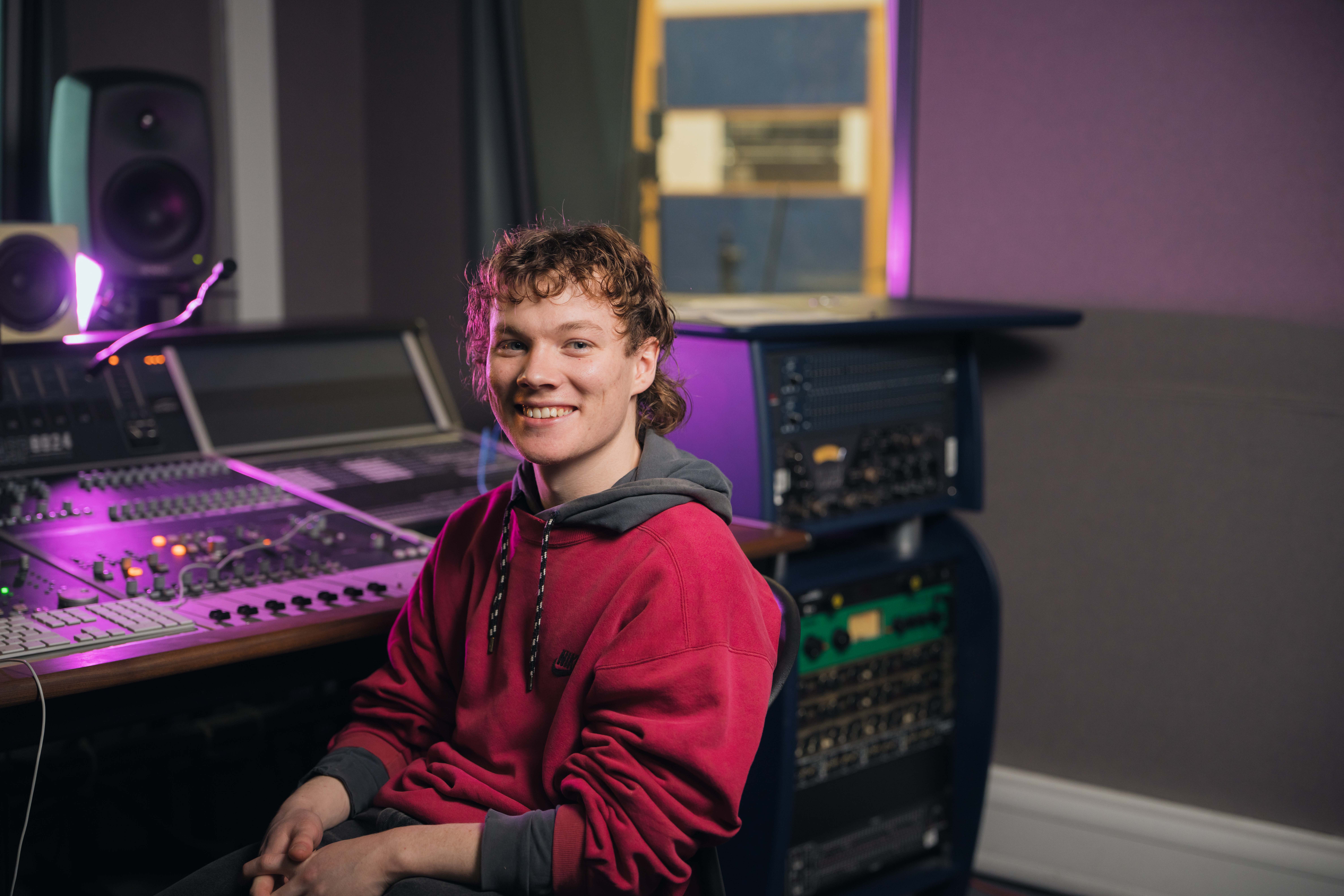 Music student sits at a mixing deck and smiling at camera