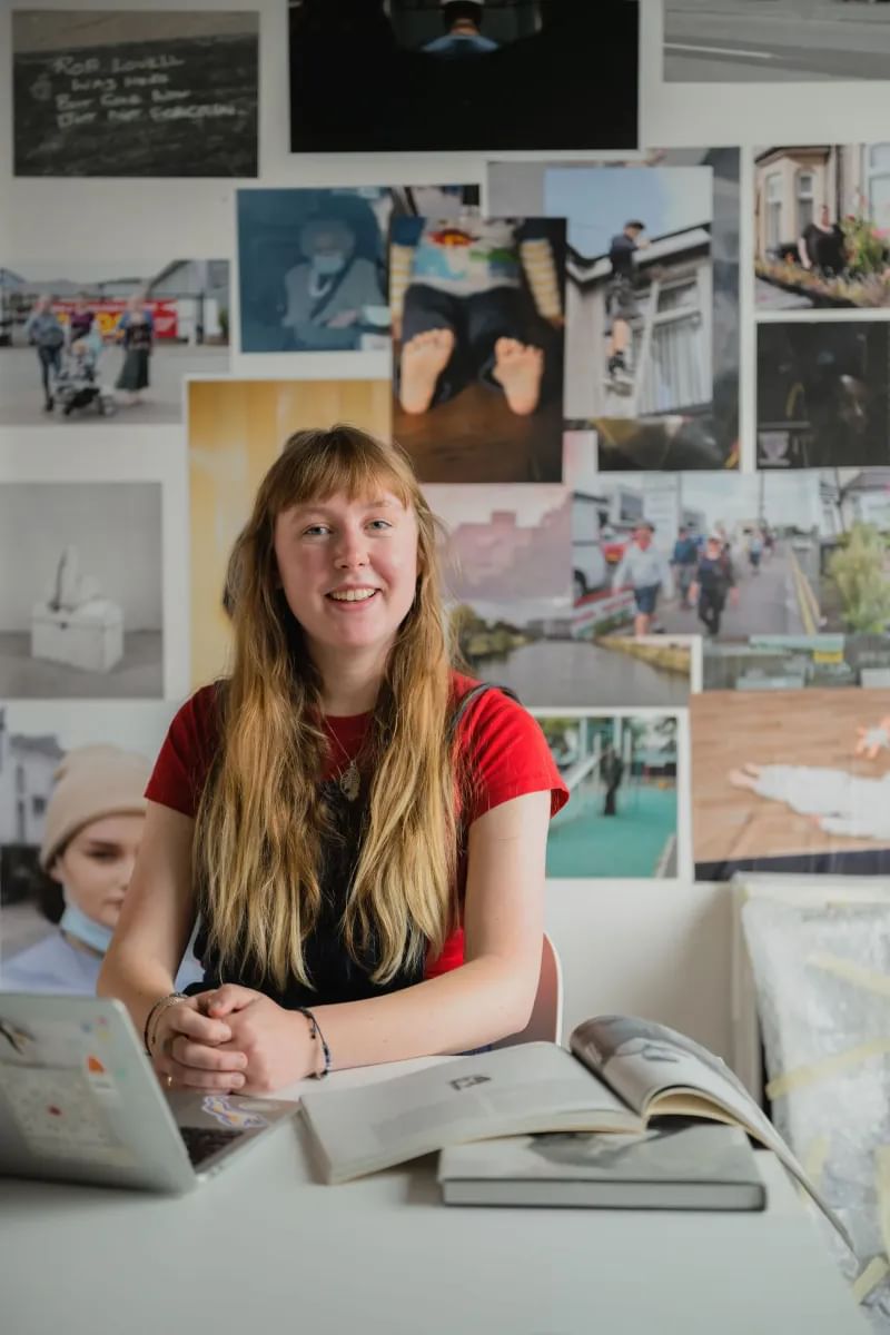 Student, Grace, sat a desk in a photography classroom surrounded by books and photogprahs on the wall
