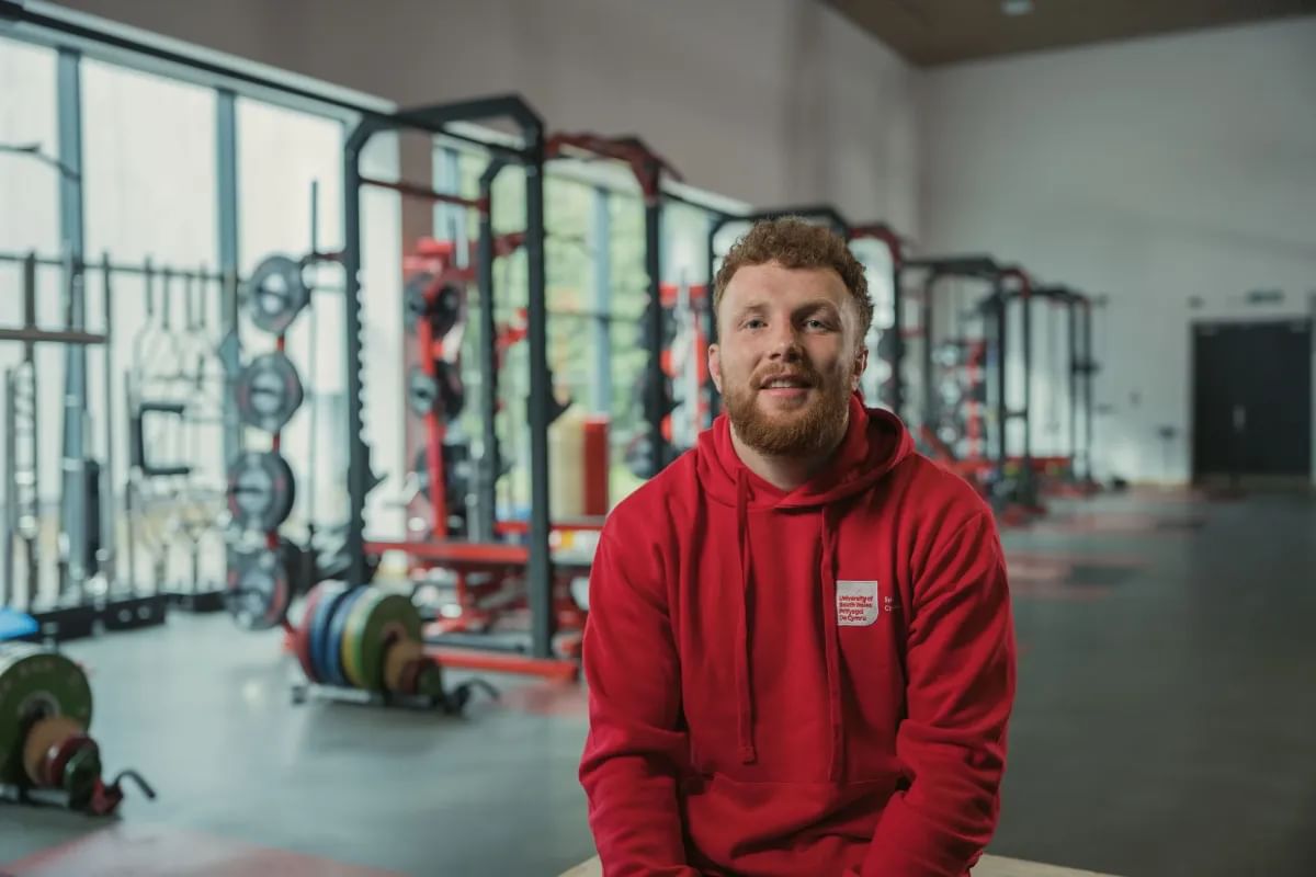 Sport student, Aneurin, sits in front of the equipment in the strength and conditioning room