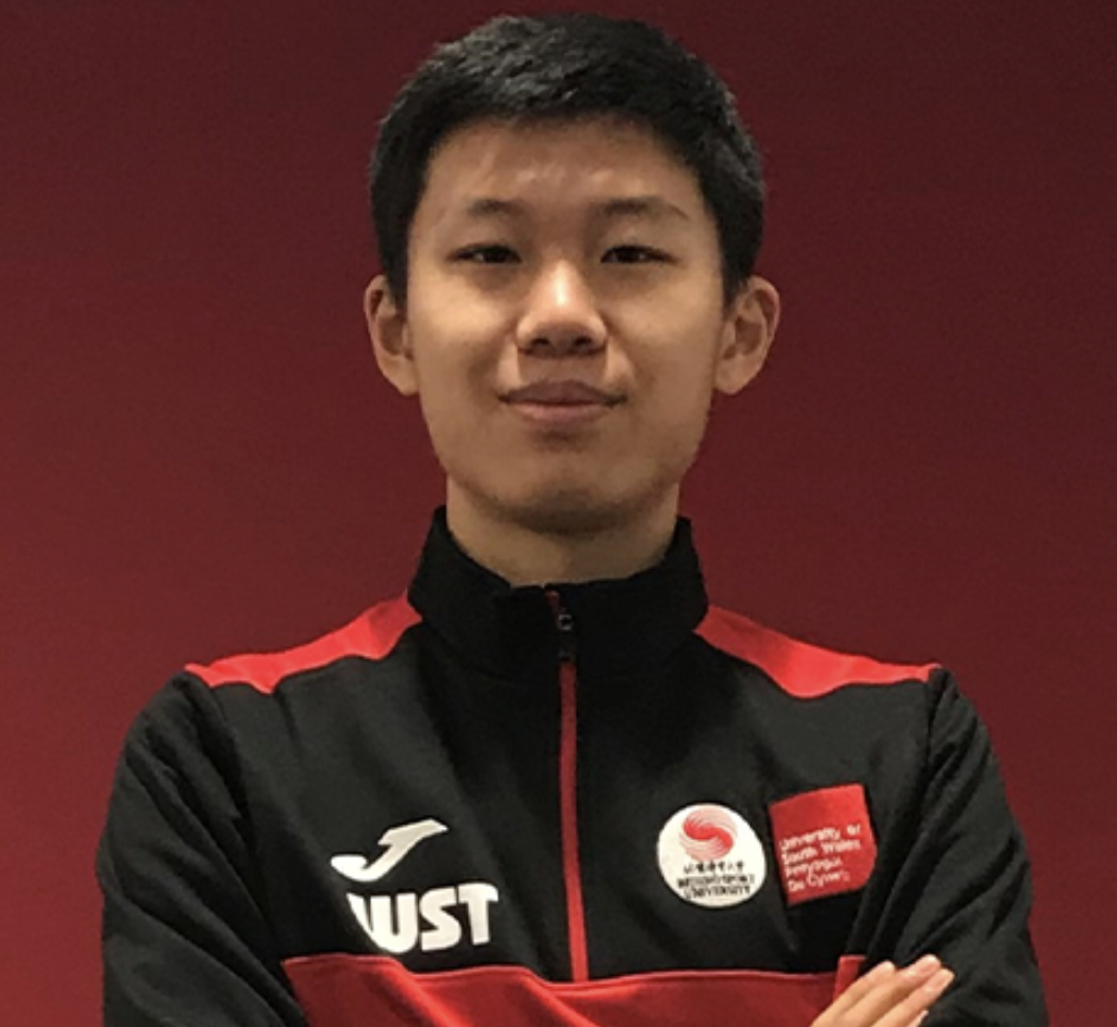 MSc Sport student Siteng Wang smiles at the camera with their arms crossed in front of a red backdrop