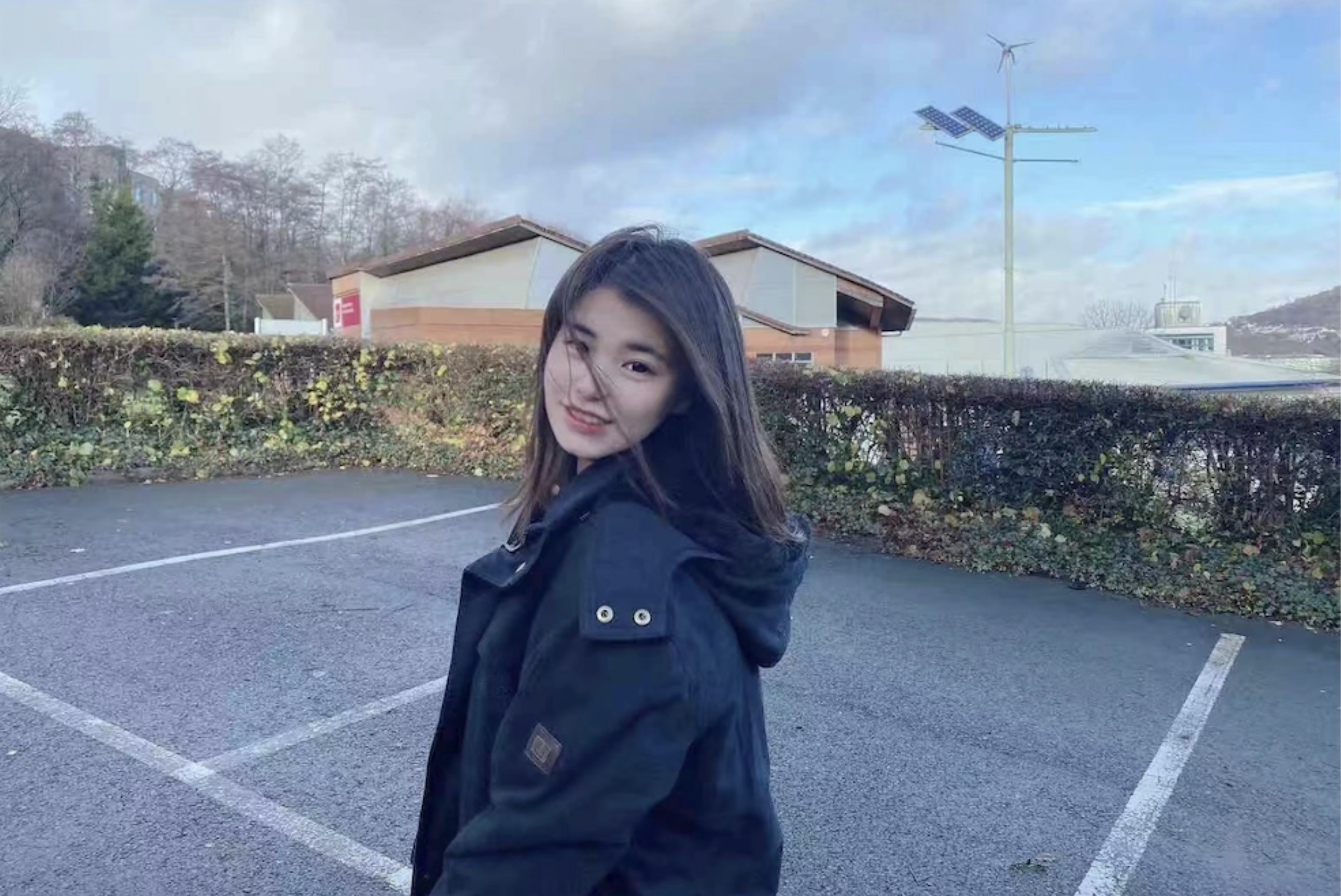 MSc Management student Xiwen Li smiles over their shoulder at the camera in a carpark with a blue sky in the background