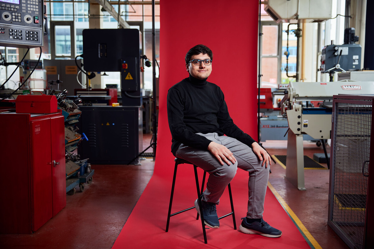 Student Musab Kazi sitting in front of red backdrop with engineering equipment in the background