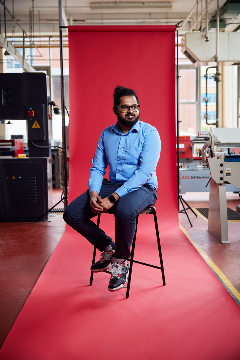 Student Vignesh Pathmaraj sitting in front of red backdrop looking off camera with engineering equipment in the background