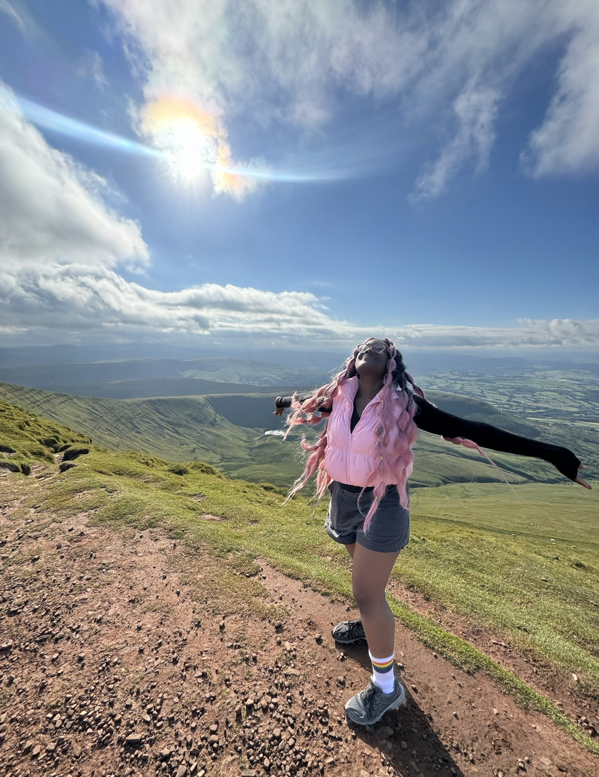 Temilorun at the top of a mountain smiling with her arms spread wide and blue skies in the background