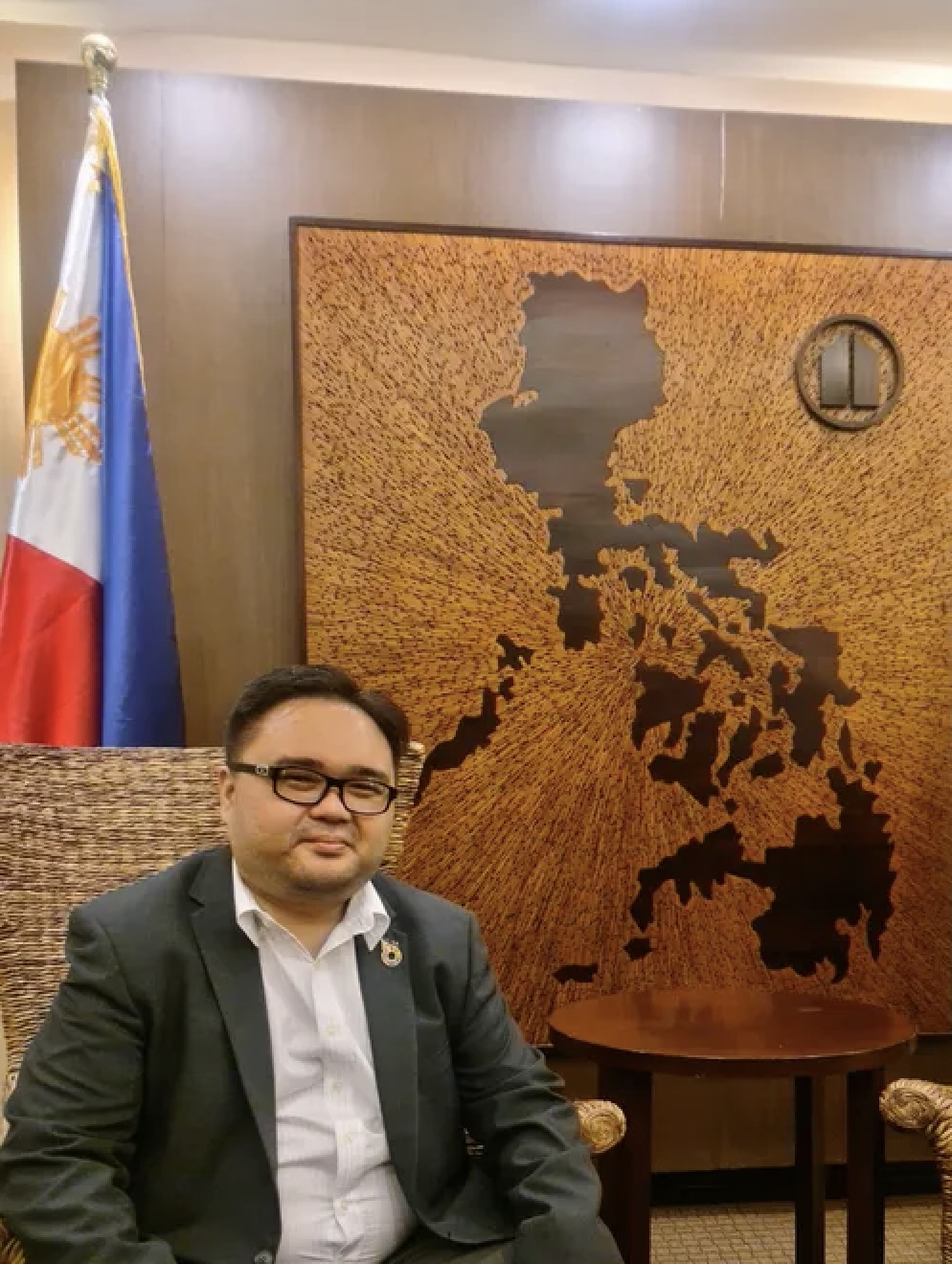 Jonas smiling at the camera with a map and flag of Philippines in the background.
