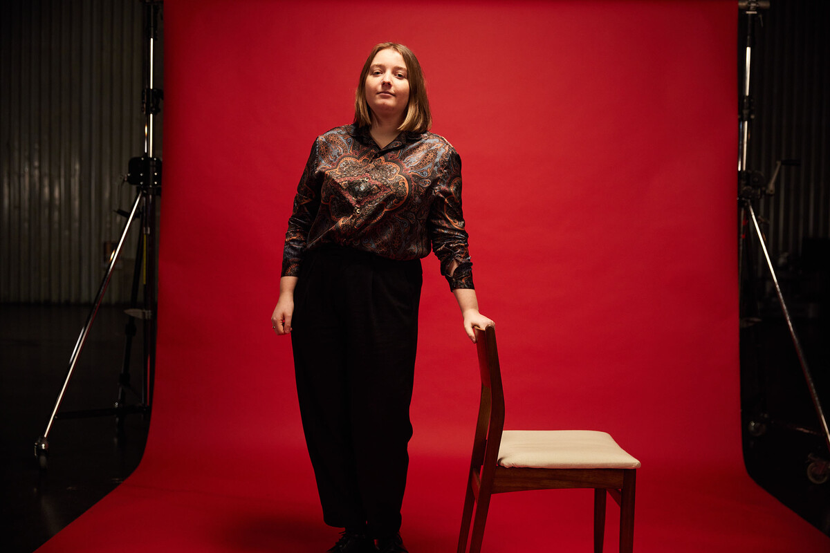 Computing alumni, Niamh, leaning on the back of a chair in front of a red backdrop