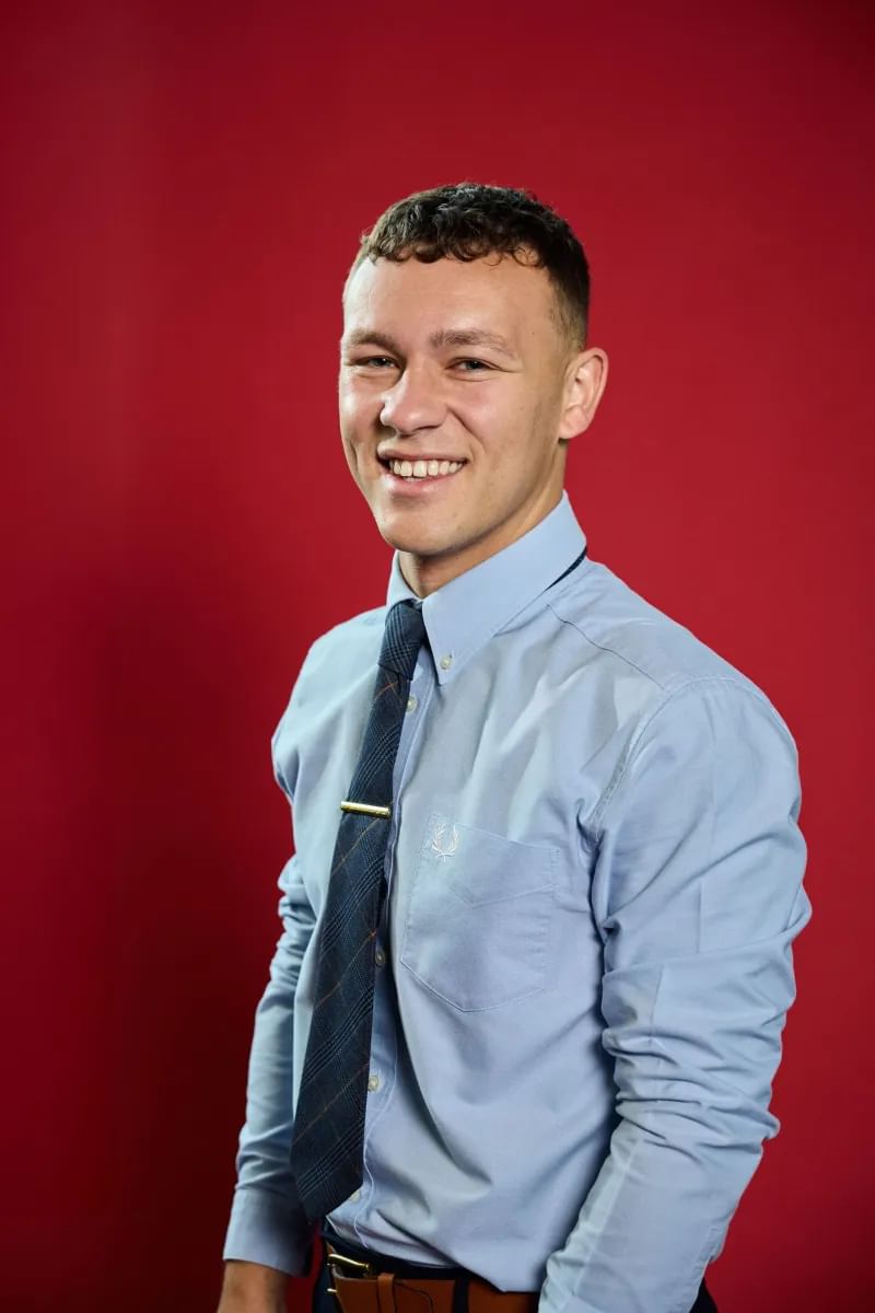 Criminology alumni, Euan, poses for a profile shot in front of red backdrop