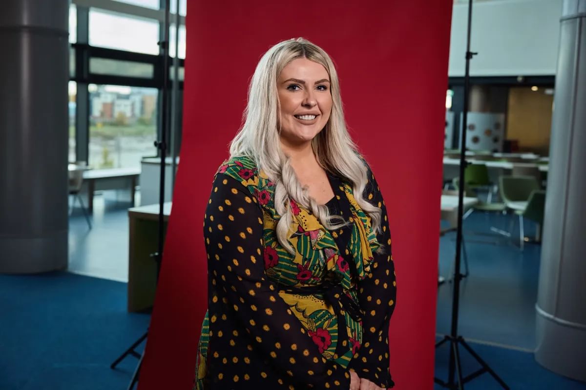 Social Work alumni, Ellis, smiles in front of red backdrop