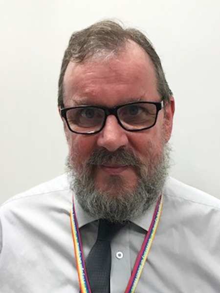 John Liscomb, Chaplaincy's Administrative Officer at USW smiling to camera standing in front of a white background