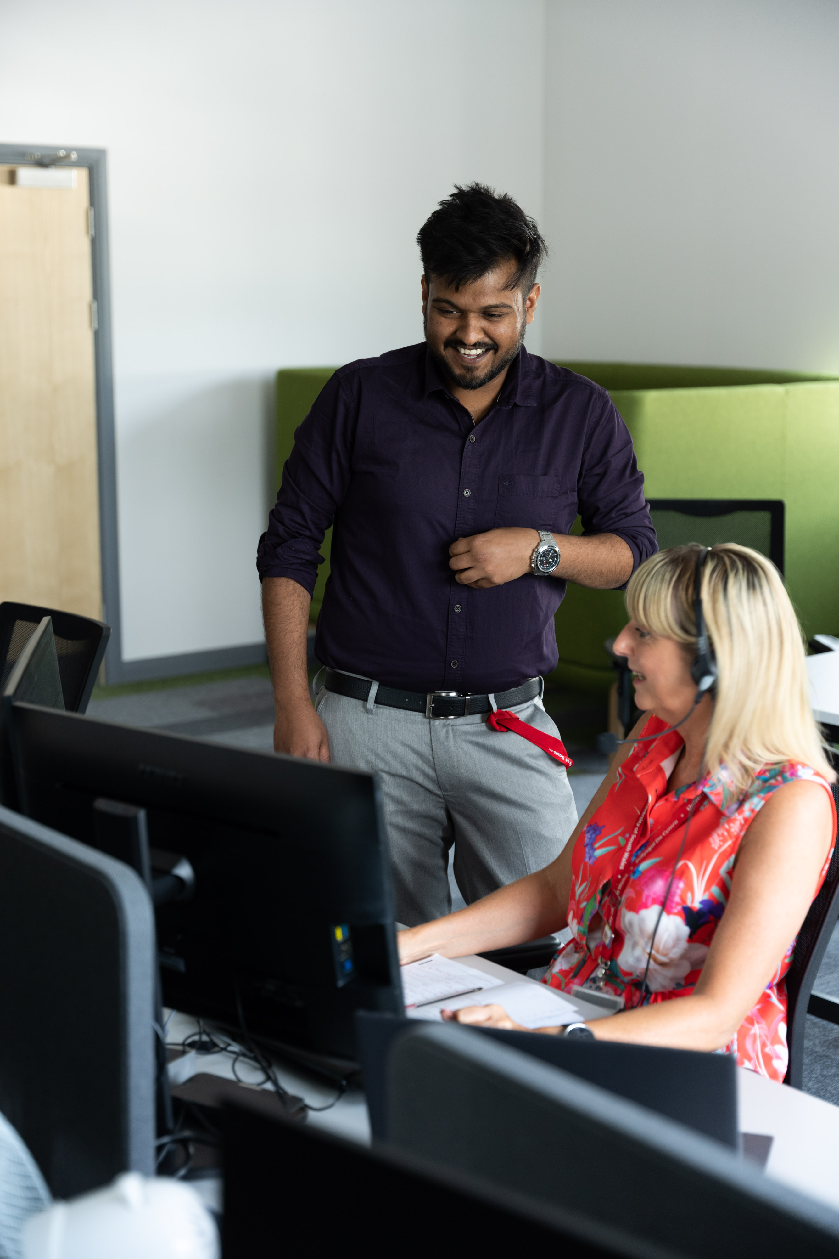two members of University staff, one sitting and one standing, looking at a computer and smiling