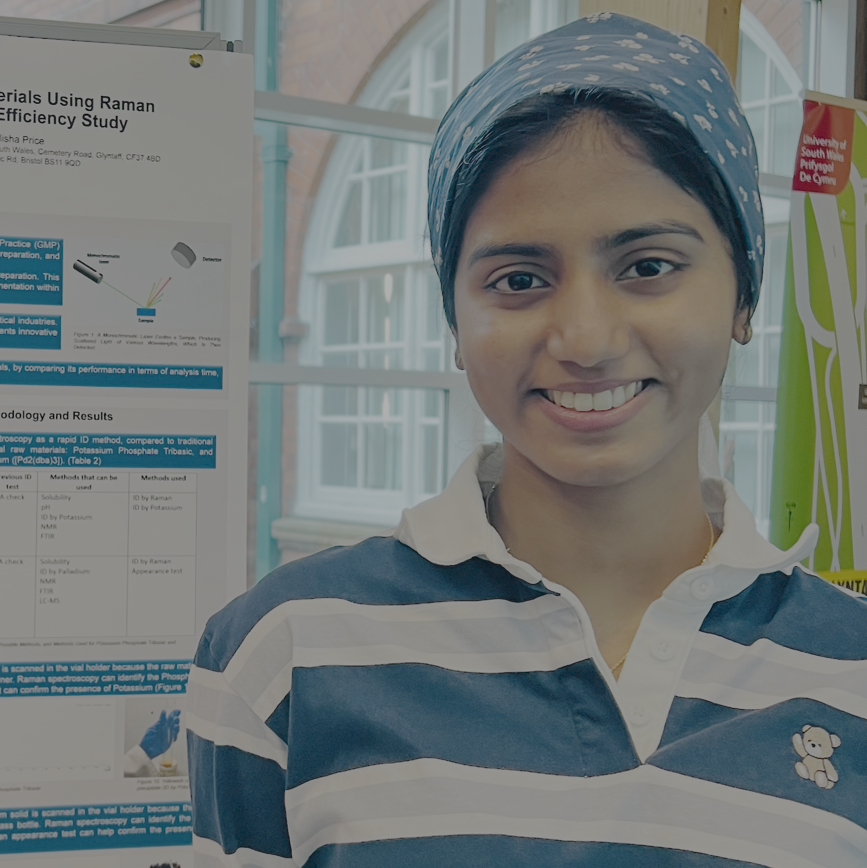 Student Senushi Jayasinghe smiles at the camera while stood in front of a USW biotech poster