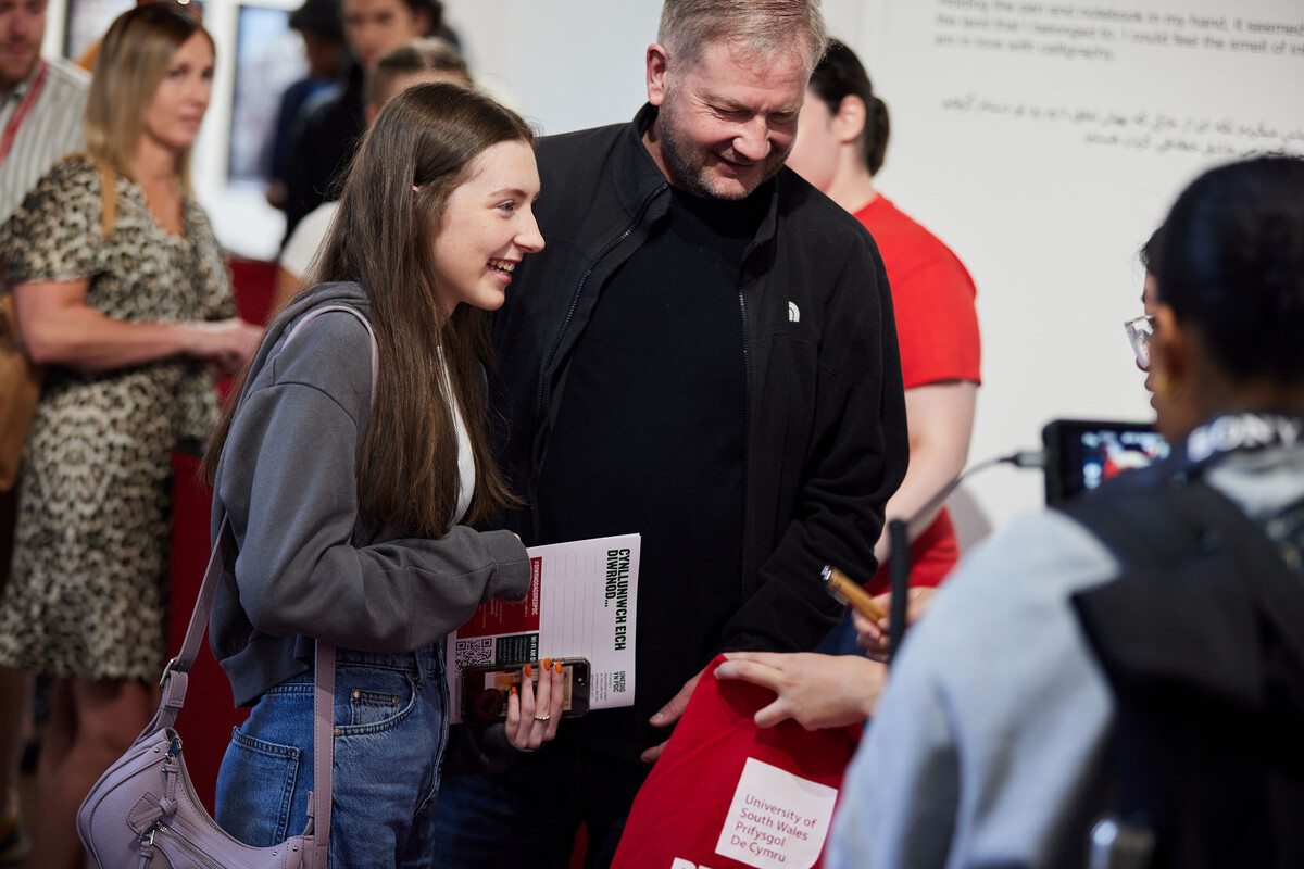 A prospective student with their parent smiling and talking to a lecturer