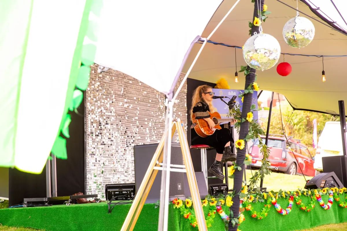 Singer performing with a guitar on stage at a campus welcome event under a tent in Treforest.