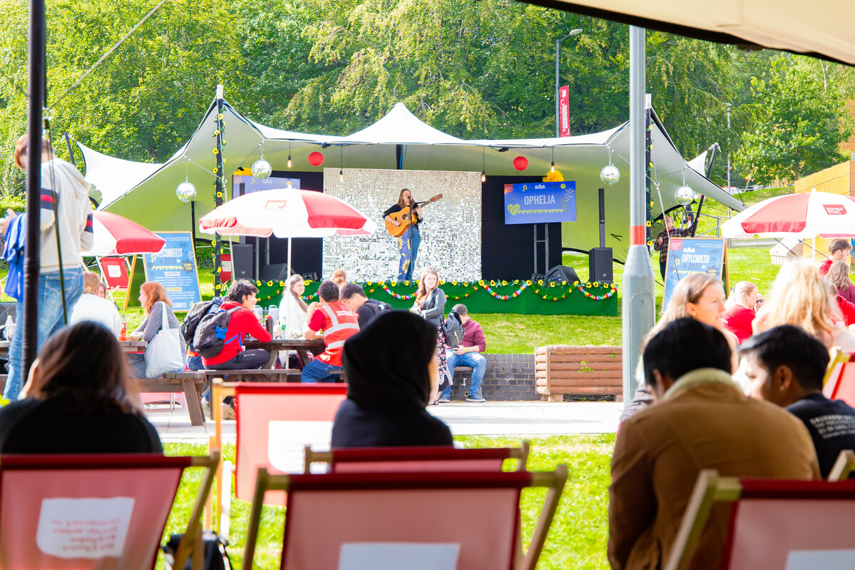 A group of students sat in the sun watching a music performance on stage at Treforest Welcome Fest