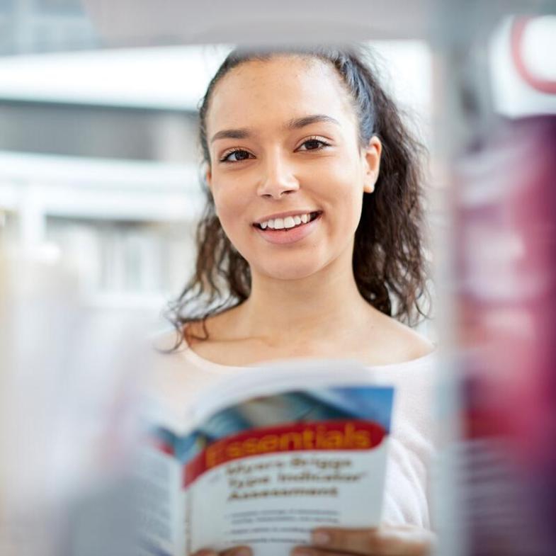 A student standing in the campus library smiling to camera
