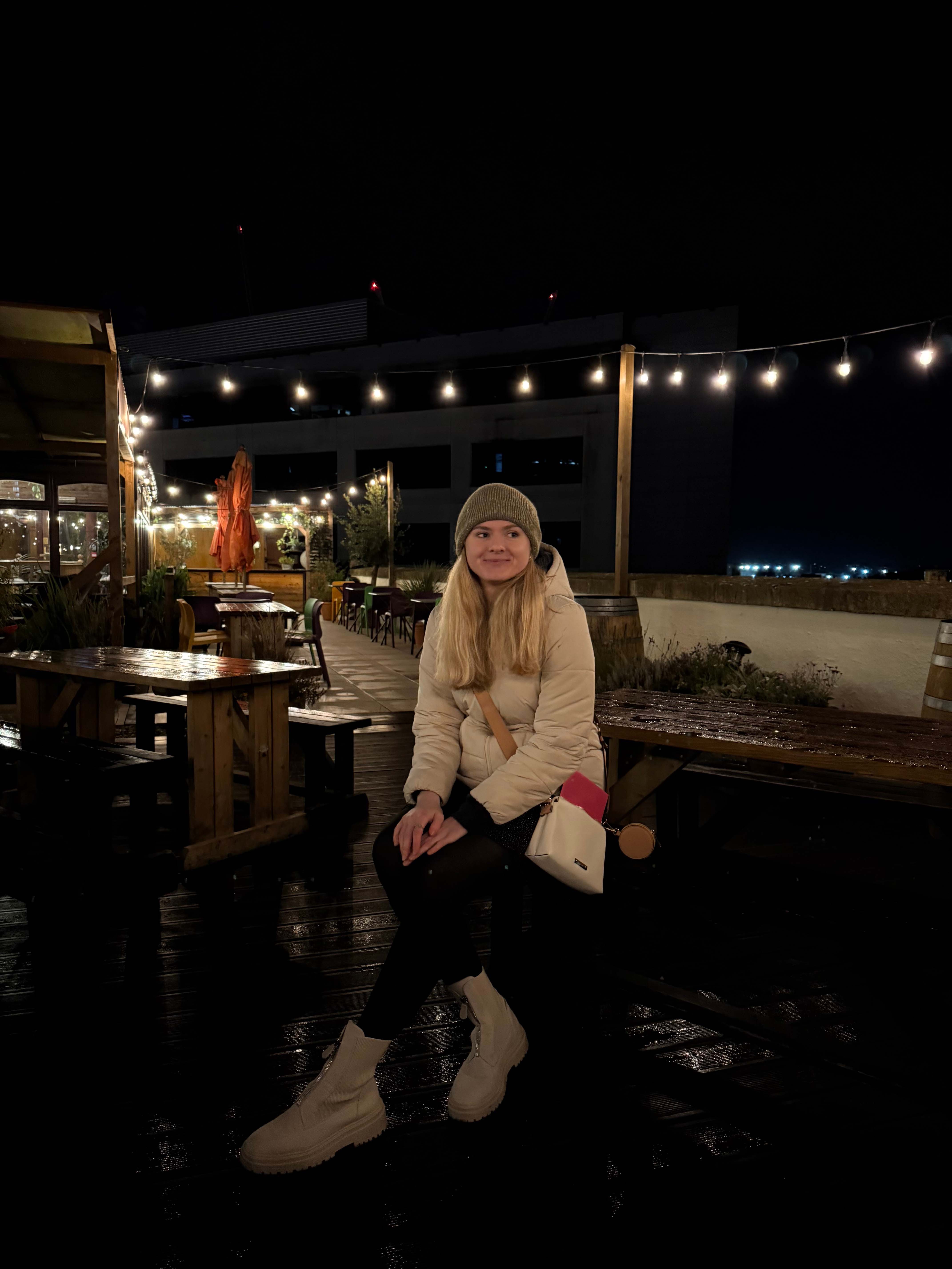 A photo of student content creator, Jade, sitting on a picnic bench with festoon lights on in the backrgound.