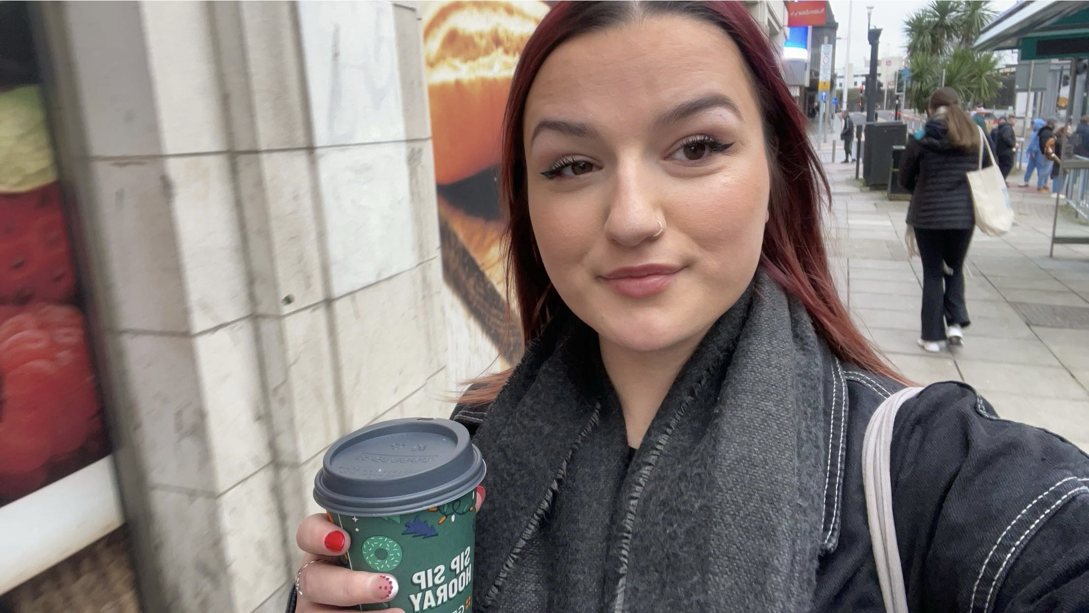 A selfie of student, Maddi, smiling and holding a takeaway coffee in Cardiff.