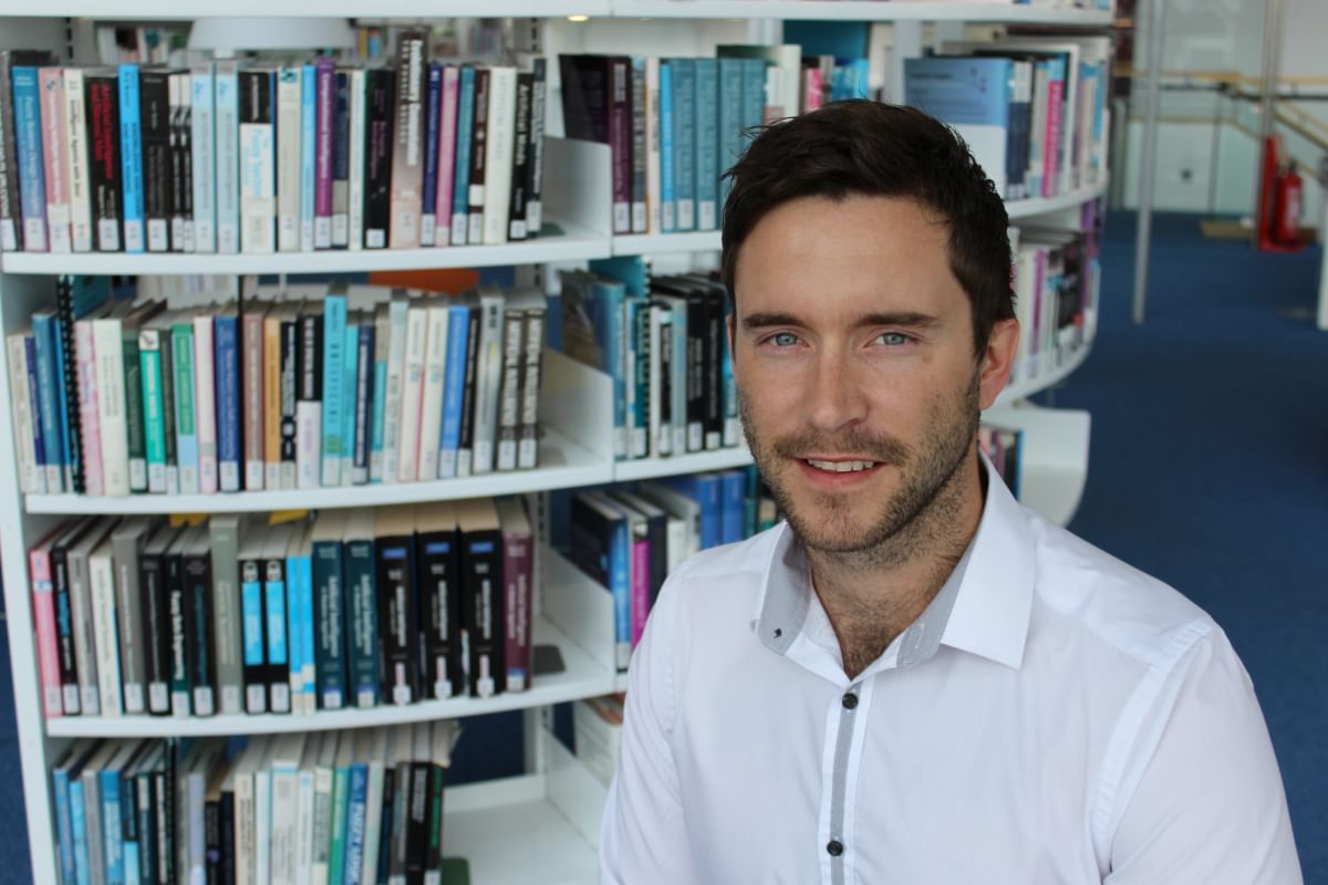 Student, Tom, poses for a profile shot in Newport campus library