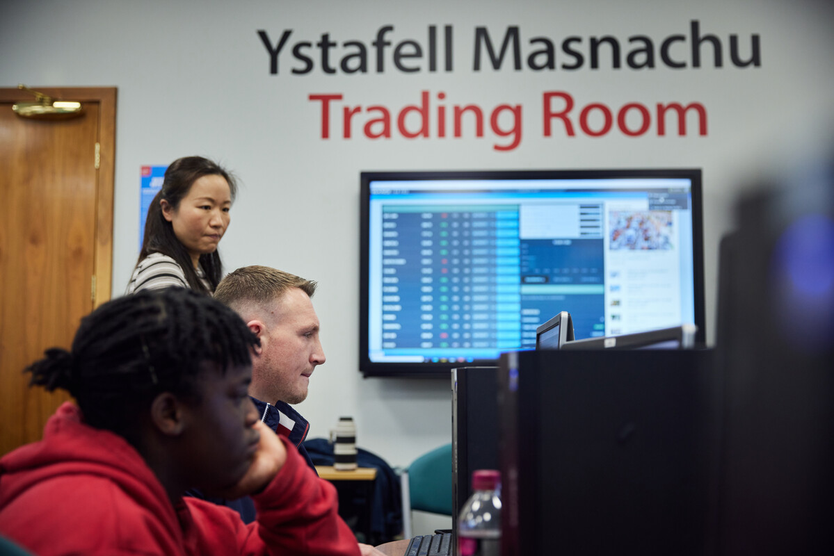 Lecturer surveying students in the Trading Room, accounting data is displayed on the classroom board.