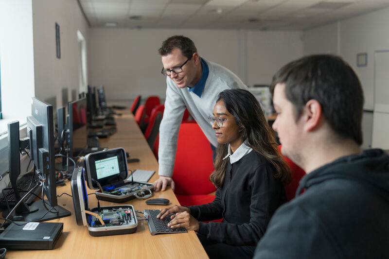 Two students and a lectuerer are gathered around a computer.
