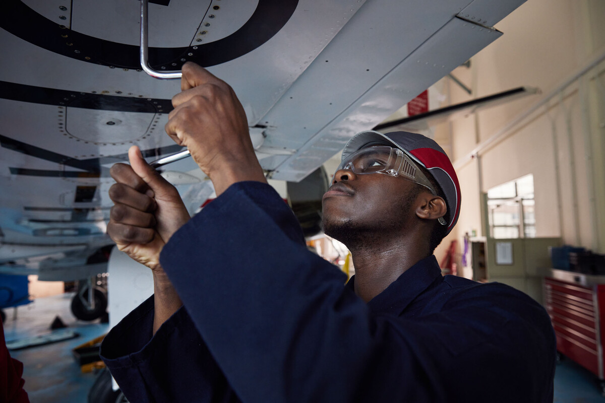 A student is standing under the wing of a plane unscrewing some bolts.