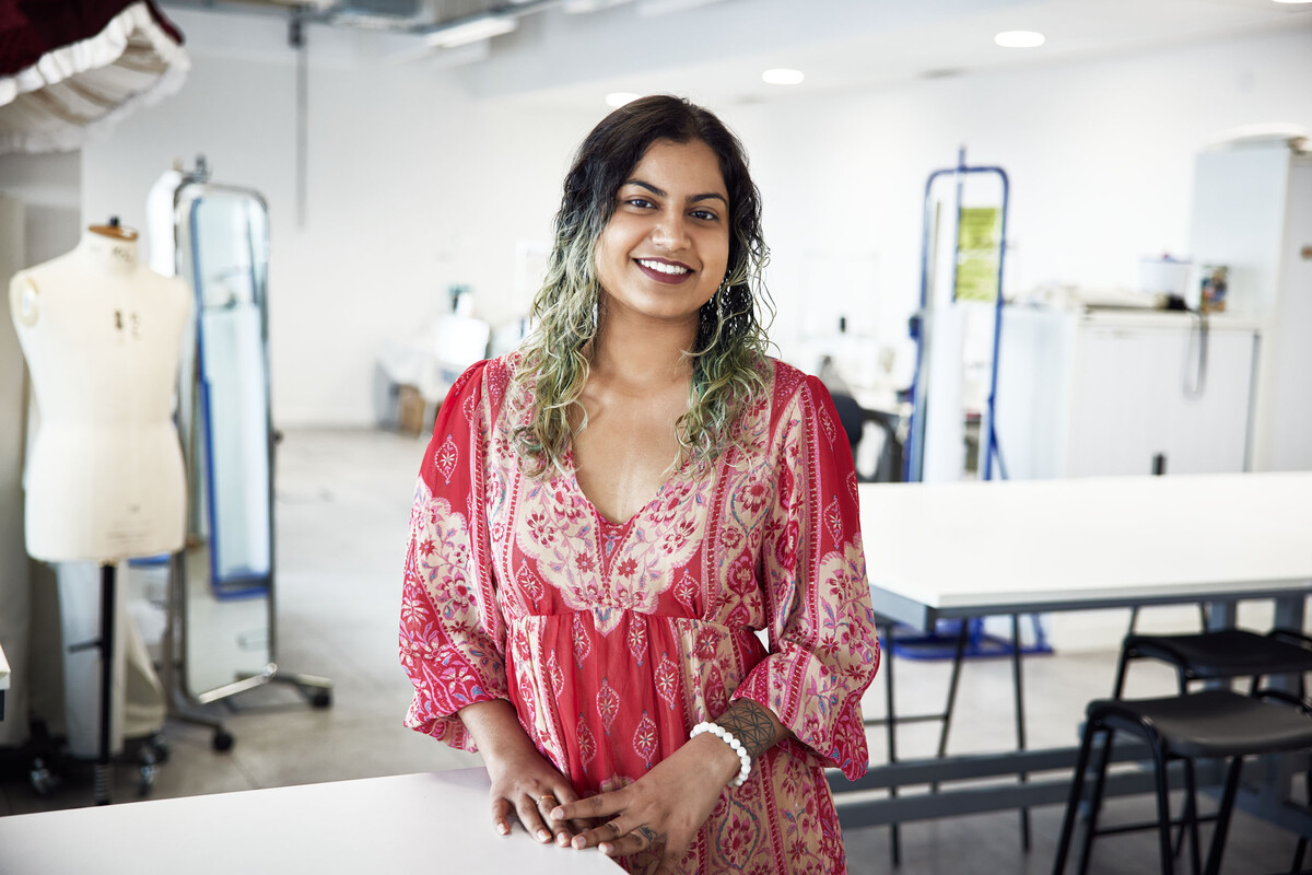 Student smiling into camera, in the background there is a mirror and tailors mannequin.