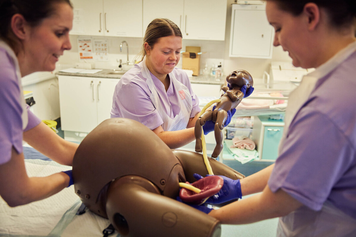 Three Midwifery students are carrying out a dummy  delivery activity.