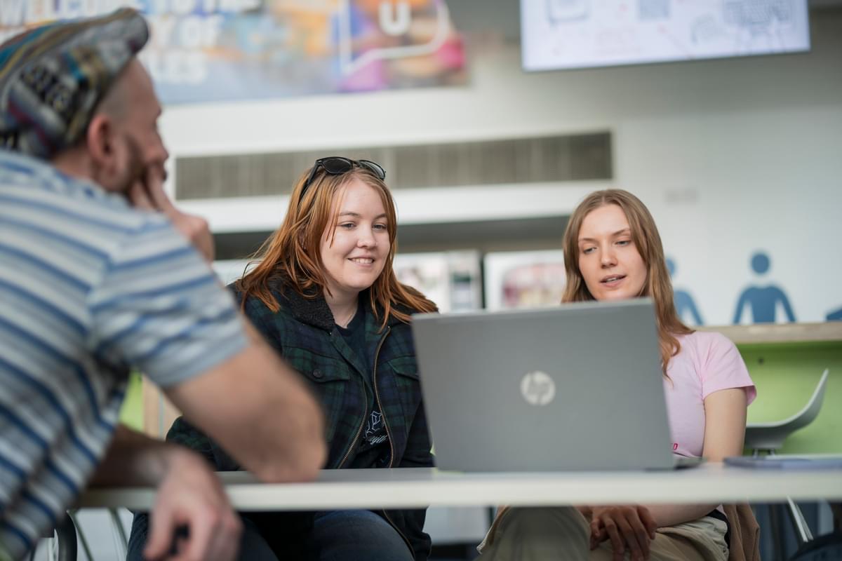 A group of students gather around a laptop while sat at a table in a communal area of USW Newport campus