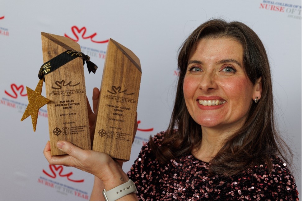 Annie, a nursing student, proudly holds two awards in front of a decorated wall.