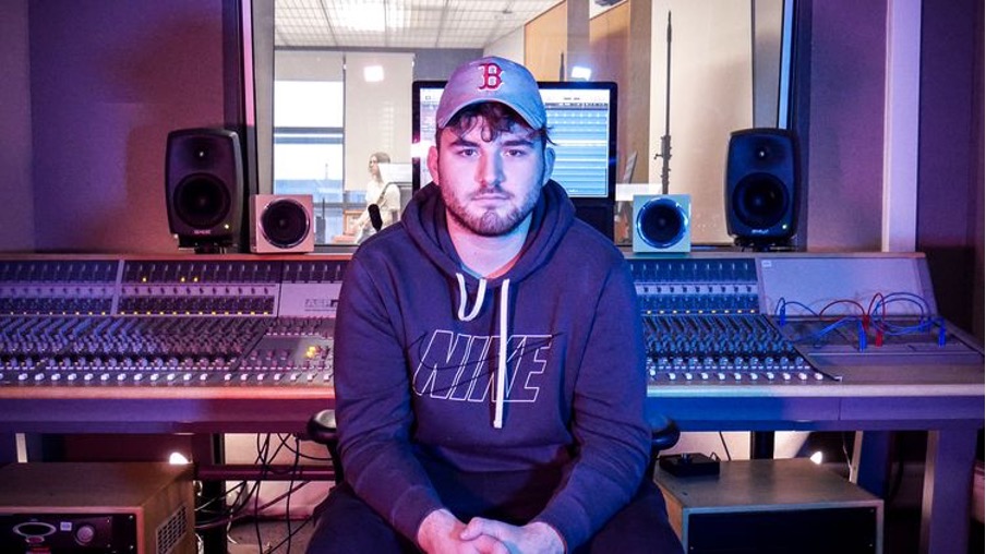 Music student, Joe, sits with his back to a mixing board in a music studio