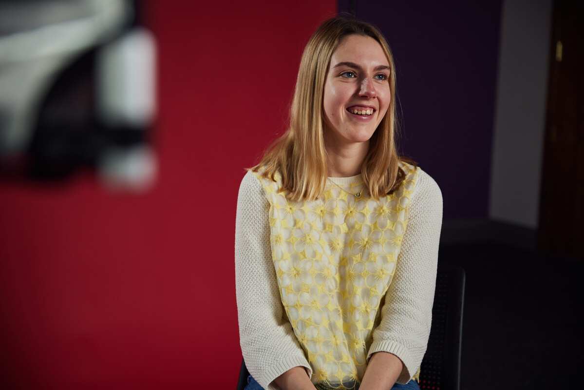 Lowri Connick sitting in front of a red background smiling off camera