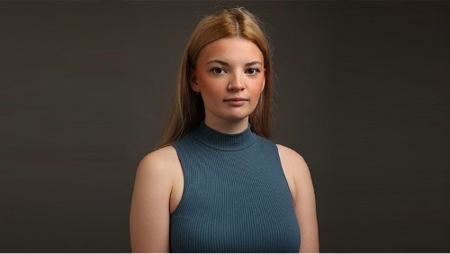 Drama student, Niamh, poses for a headshot photo. She is wearing a blue vest and is looking directly at the camera