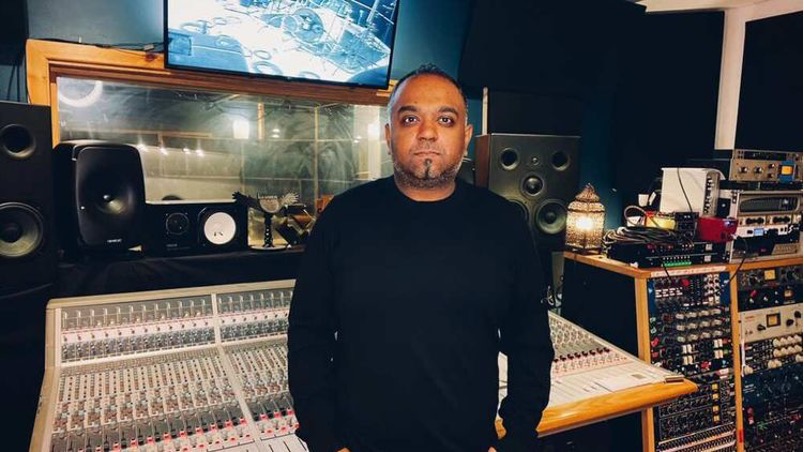 Romesh, grammy-nominated producer, stands proudly in front of a mixing board in a music studio