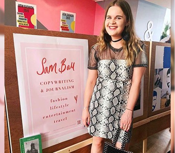 Fashion graduate, Sam, stands in front of sign to her copywriting event