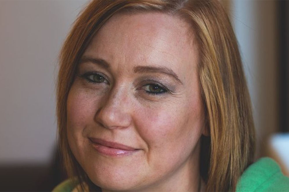 Emma smiles for a photograph, wearing a green jumper