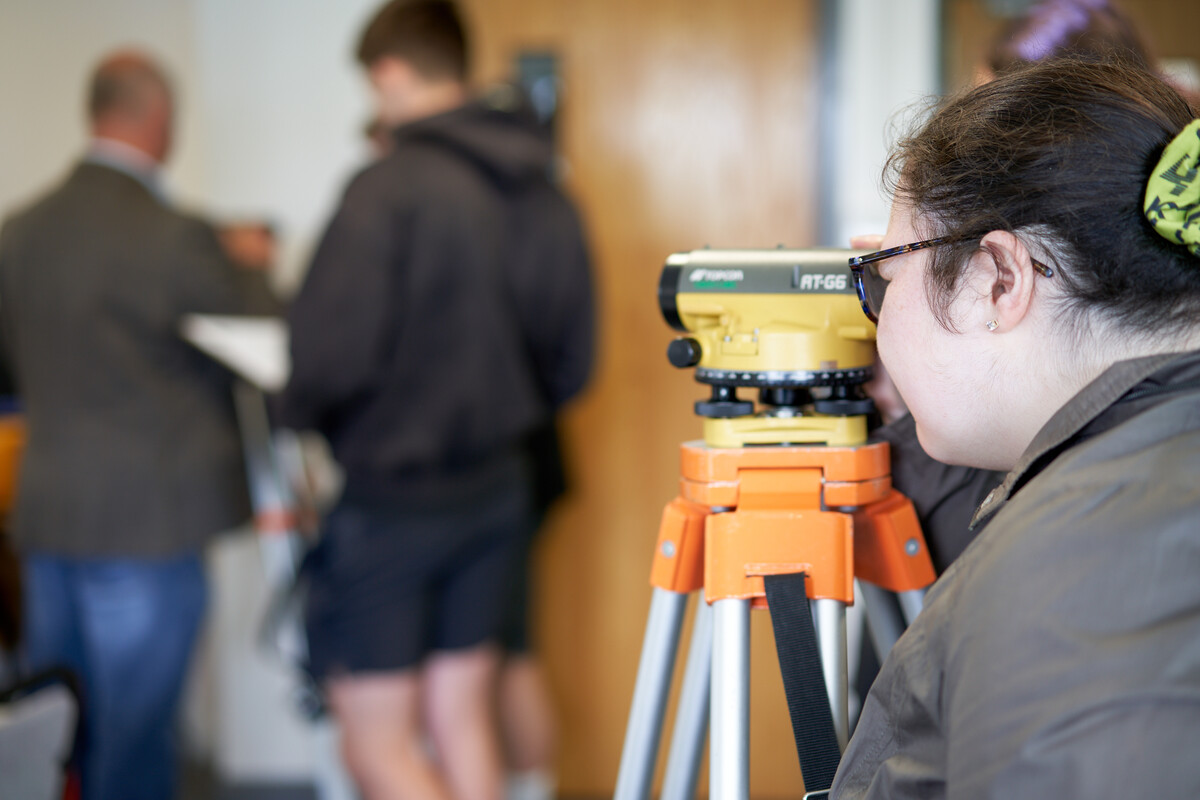 A school pupil looks through a piece of surveying equipment with other pupils in the background inside a USW classroom