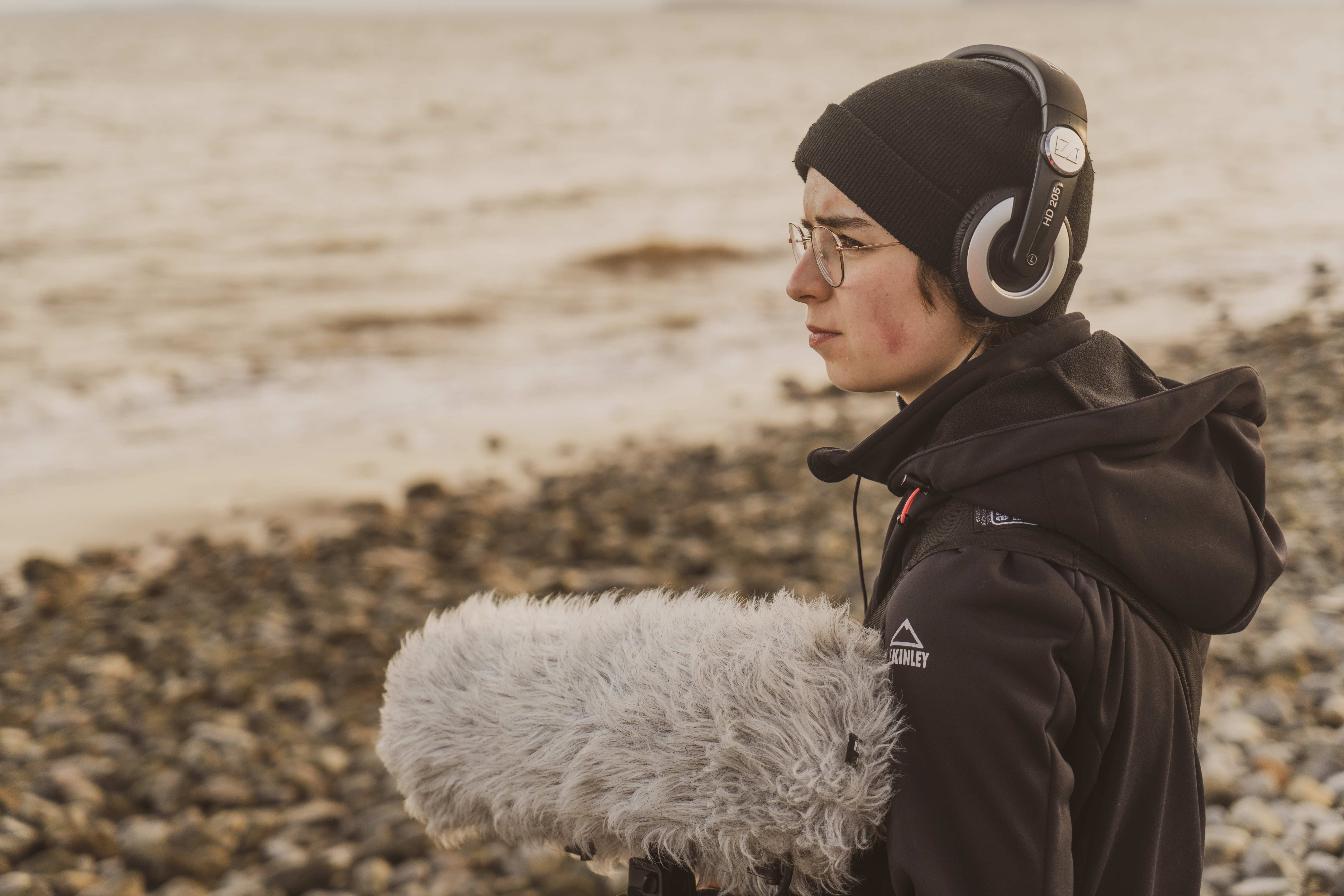 media student standing on a beach with sound recording equipment