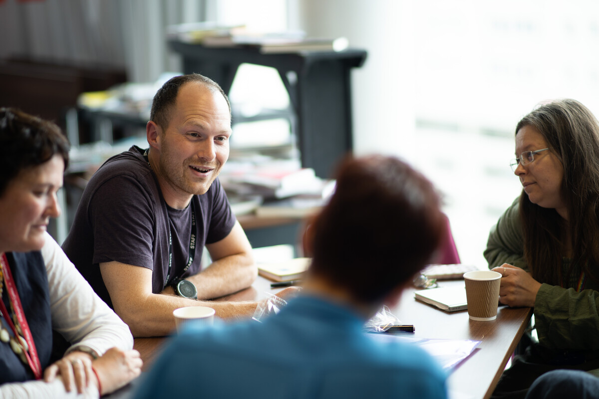 A group of researchers sit around a table chatting with coffee and books