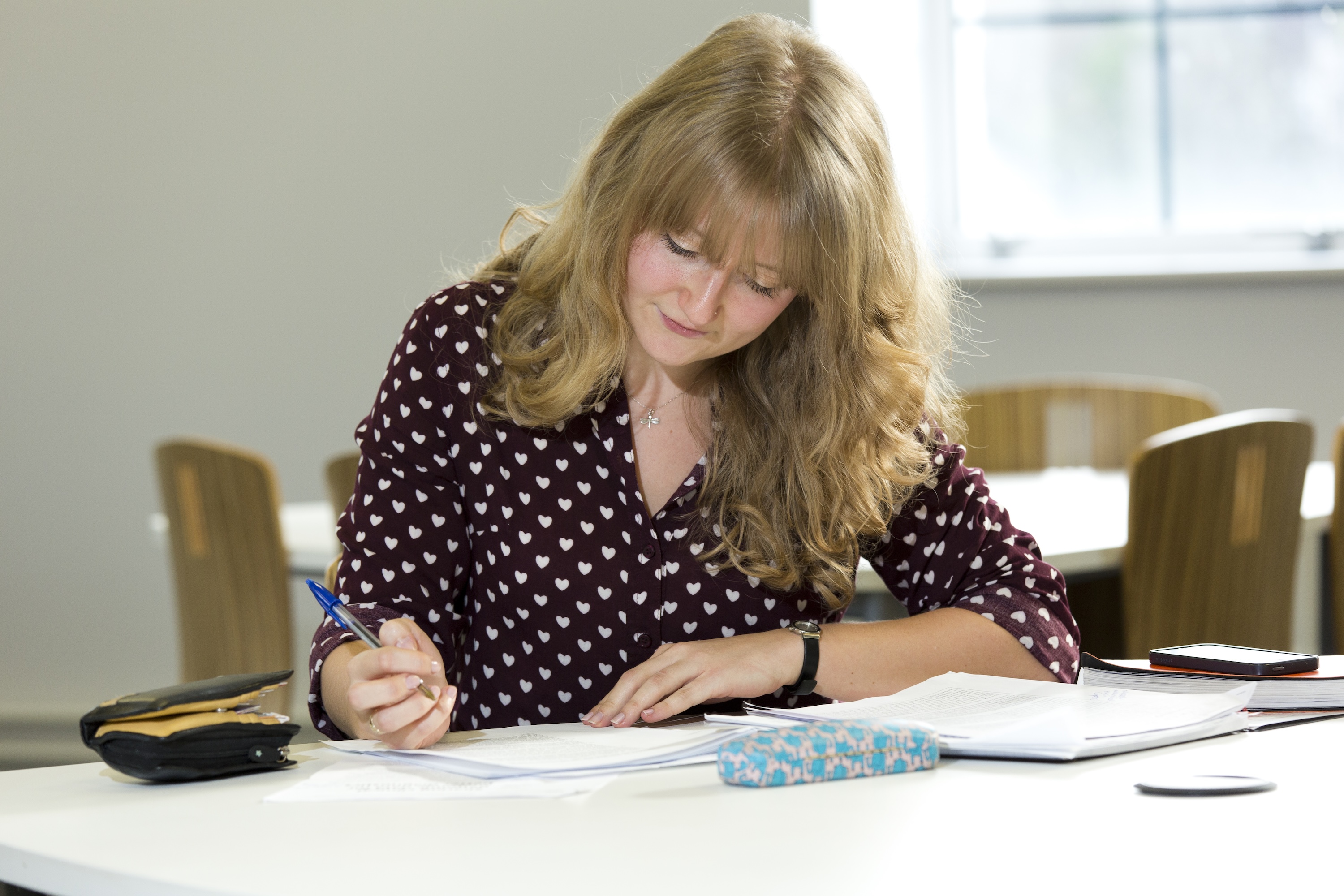 PhD student Sophie John concentrating while writing in a notepad on a desk in a student area