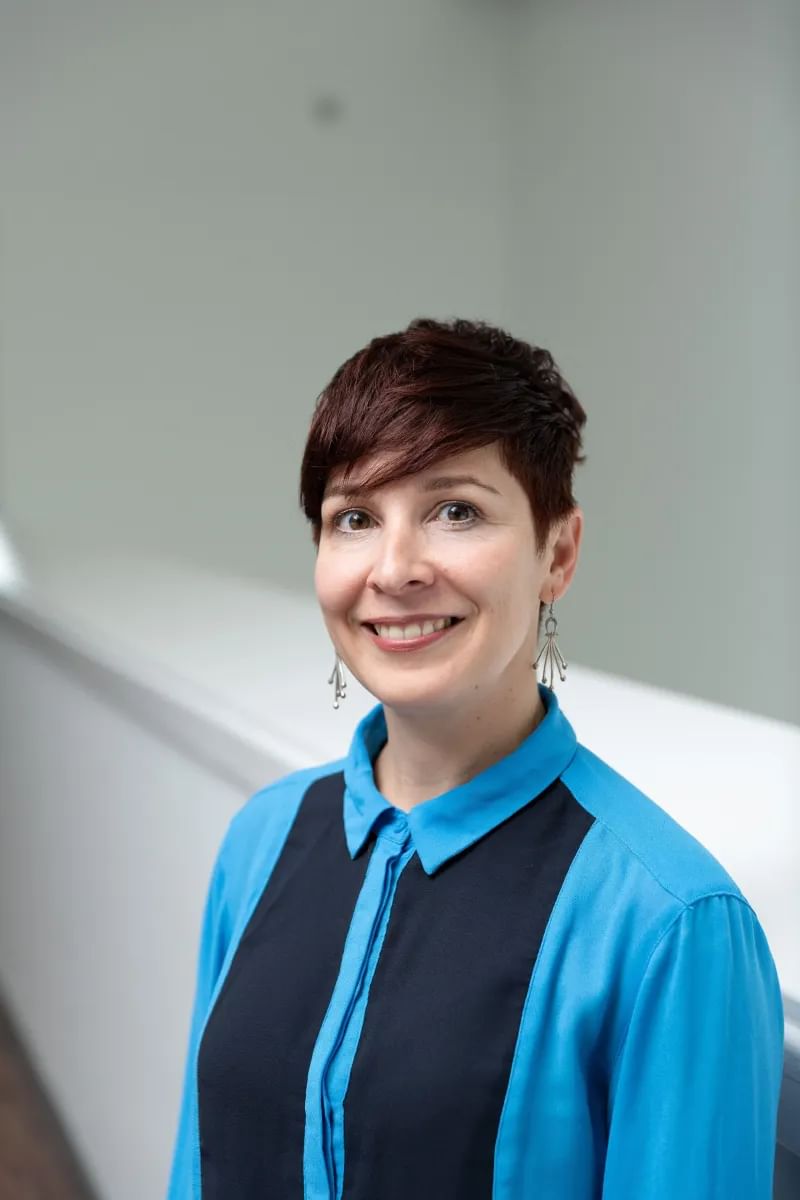 a headshot of a person with cropped hair, wearing a blue shirt